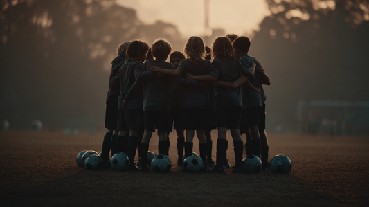 A team of youth soccer players in a huddle with soccer balls around them on the pitch.