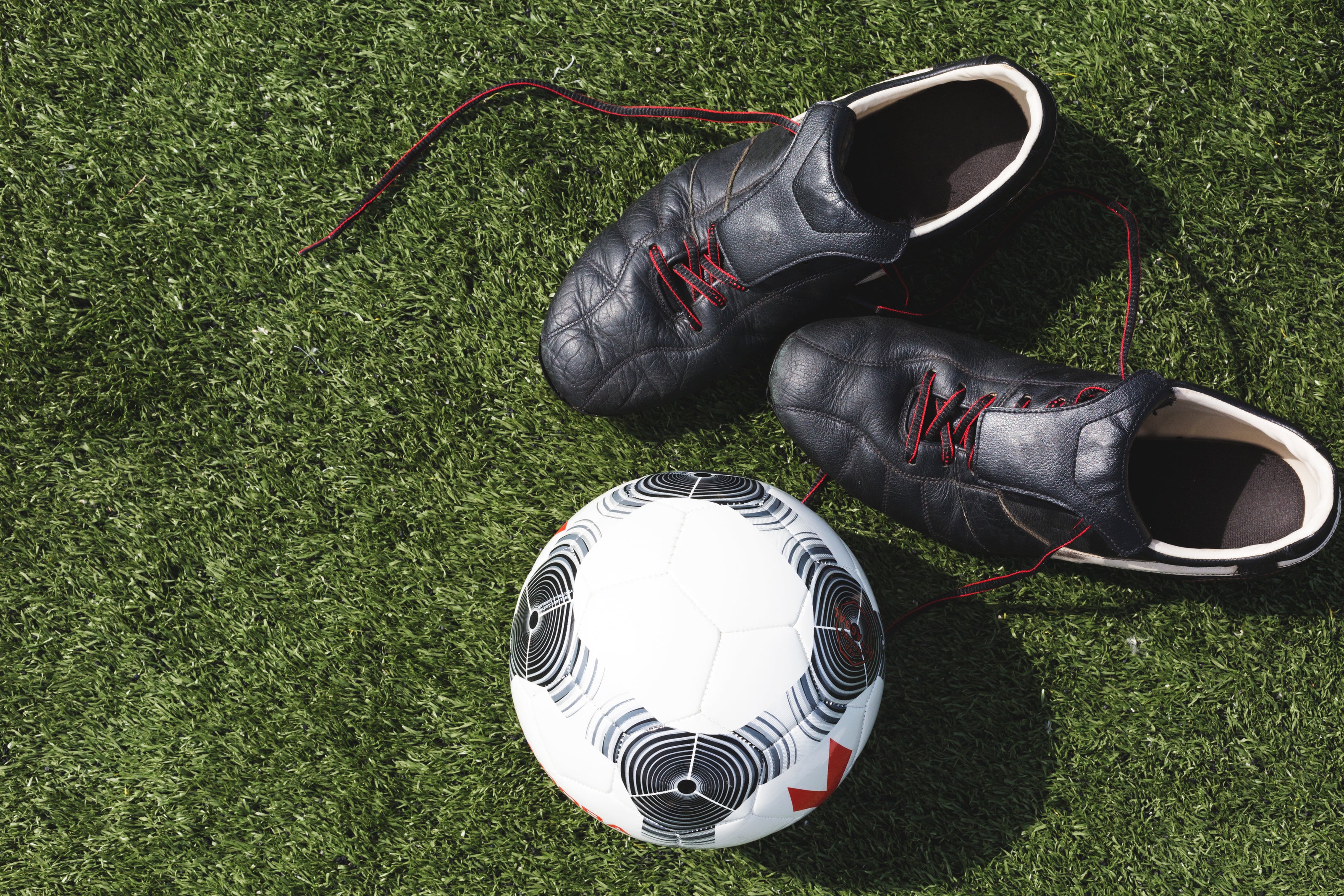 A picture of two soccer boots next to a nice soccer ball on a turf soccer field.